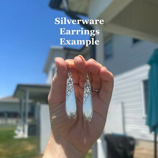 Hand holding silver silverware earrings with a blurred outdoor background