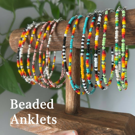 A collection of colorful beaded anklets with clasp, displayed on a wooden holder, with a variety of colors and patterns.