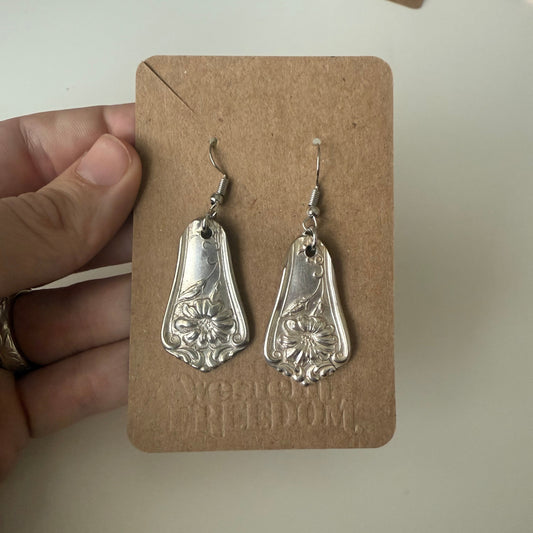 Silver earrings on a cardboard backing held by a hand.