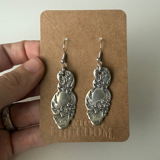 Silver earrings on a brown card held by a hand against a plain background