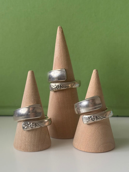 Three silver rings displayed on wooden cones against a green background